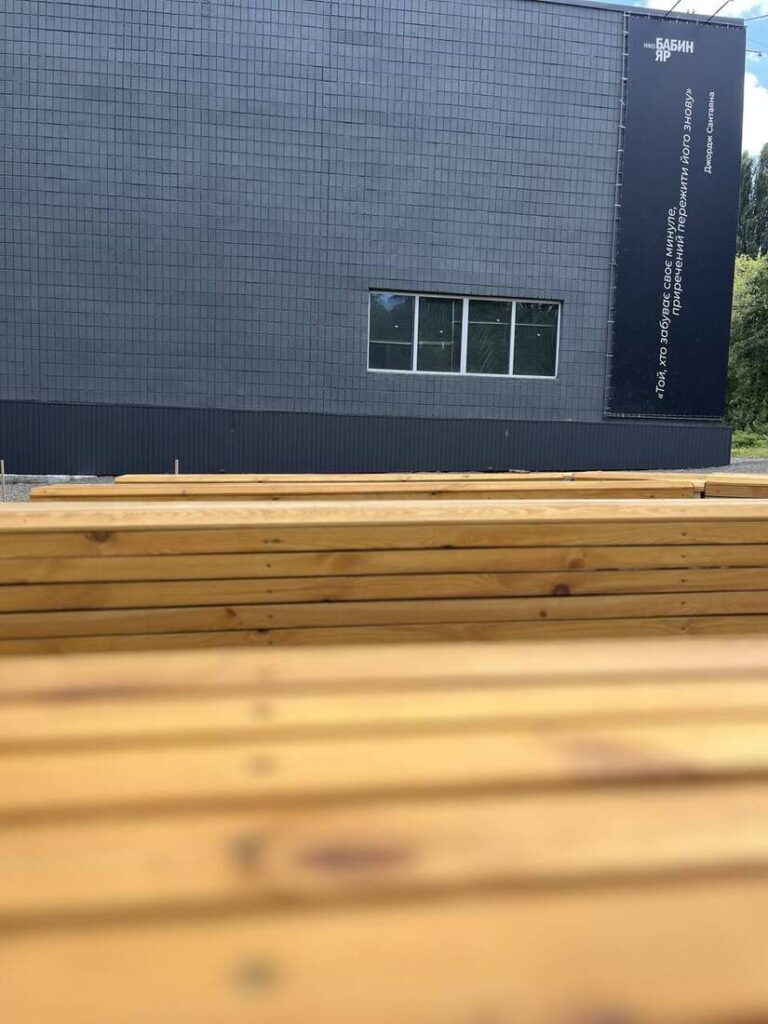 Дерев’яні лави крупним планом на тлі будівлі заповідника
