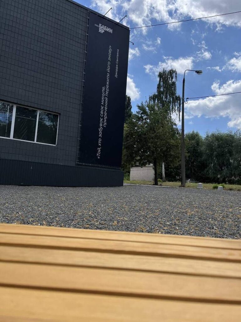 Будівля заповідника з банером-цитатою, на передньому плані дерев’яна лава